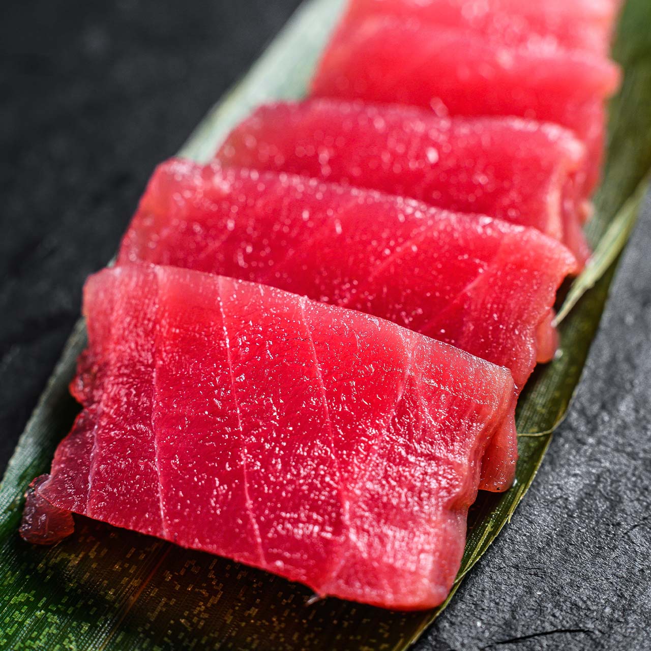 Premium whole yellowfin tuna and sashimi-grade loin slices on dark slate