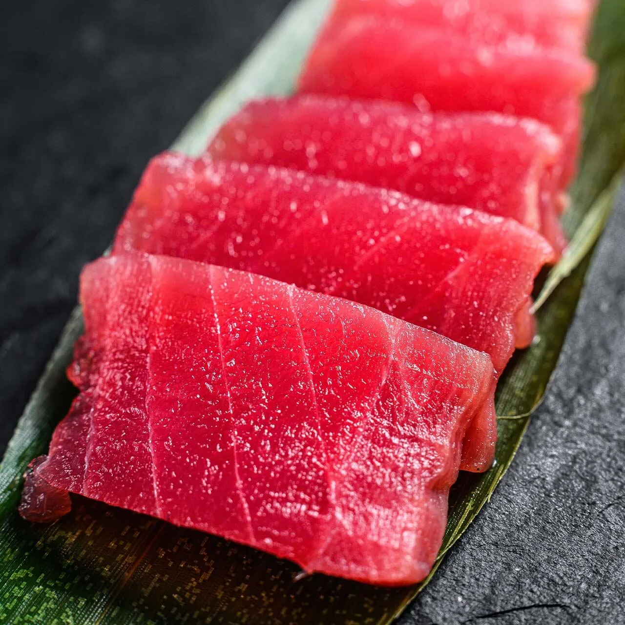 Premium whole yellowfin tuna and sashimi-grade loin slices on dark slate